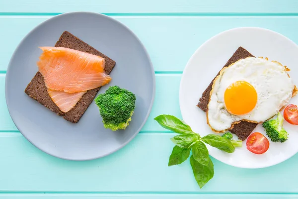 Delicious eggs with smoked salmon toasts with vegetables and greens on wooden turquoise background, top view.
