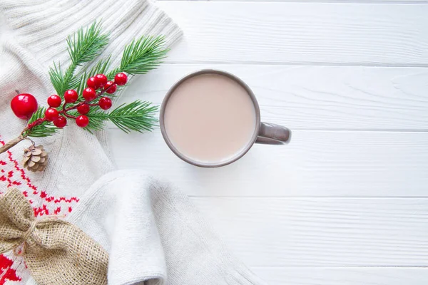 Beyaz yün süveter ve beyaz ahşap arka planda bir fincan sıcak kakao. Noel kırmızı süslemesi. Selamlama alanı, kopyalama alanı. 