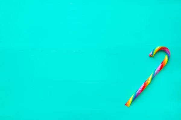 Rainbow candy stick on turquoise background. Creative trendy background, top view.