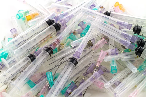 Many used syringes and needle lie strewn on a flat surface Stock Photo