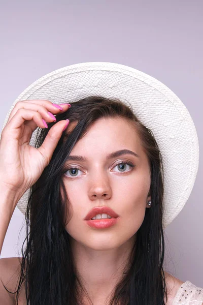 Studio gri bir arka plan üzerinde beyaz bir hasır şapka giyen genç ve güzel kadın moda