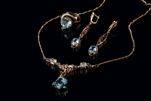 Guld halsband, ring och örhängen med ädelstenar och diamanter och topaz på svart bakgrund i studio — Stockfoto