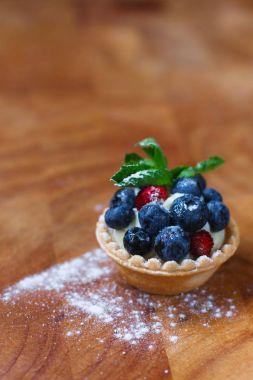 Lezzetli blueberry tart ile taze yaban mersini, çilek, nane yaprakları ve ahşap bir arka plan üzerine krem şanti. Fransız mutfağı