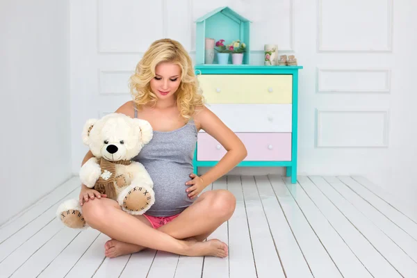 Mulher grávida senta-se e segura um urso de pelúcia — Fotografia de Stock