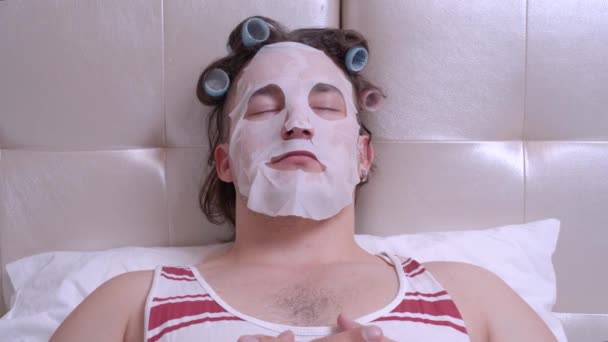 Uomo con una maschera cosmetica sul viso in una stanza, apre gli occhi bruscamente, dice boo — Video Stock