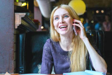 Sarışın, genç bir kadın cep telefonuyla konuşuyor ve kahkahalarla kahkahalar atıyor..