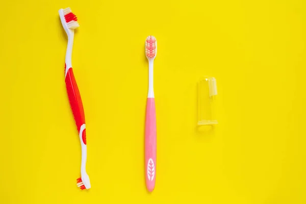 Different types of colored toothbrushes for people, dogs and pets isolated on yellow background. Daily oral hygiene on schedule for dental health. Double sided and transparent rubber finger brushes. — Stock Photo, Image