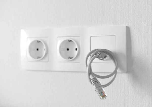 Zwei Steckdosen und Netzwerkbuchse mit Ethernet-Spiralkabel an weißer Leerwand, Seitenansicht, Nahaufnahme. Reparatur, Stromversorgung und Verkabelung in einer neuen Wohnung. — Stockfoto