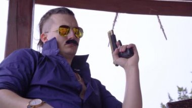 Mavi gömlekli, yakalı, güneş gözlüklü, polarize lensli havalı gangster adam silah tutuyor, namluyu kurbana doğrultuyor, bileğindeki altın saat, mafya hesaplaşmaları..