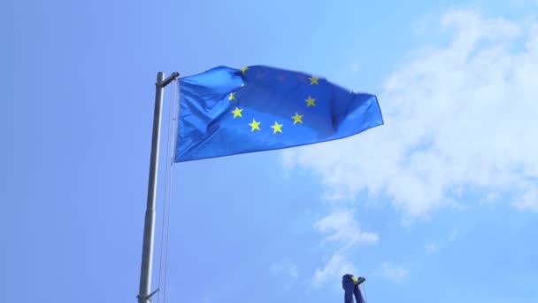 Politik ve ekonomik Avrupa Birliği bayrağı, mavi alanda on iki altın yıldızla güneşli bir günde bulutlu bir gökyüzüne karşı rüzgarda dalgalanıyor.. — Stok video