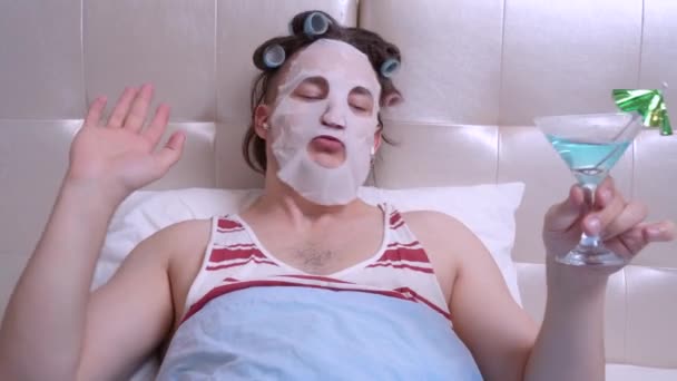 Man met een cosmetisch masker met draadloze koptelefoon met een cocktail en dansen — Stockvideo