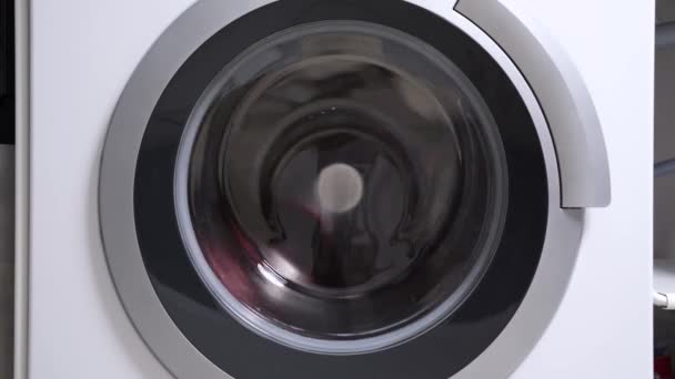洗衣机的闭式滚筒旋转缓慢，用织物柔软剂冲洗脏脏的多色洗衣房，关闭。大型家用电器的广告，用于房屋的一般清洁. — 图库视频影像