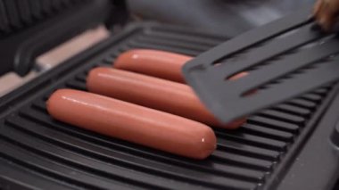 Elektrikli ızgarada kızartılmış üç sosis ve plastik mutfak spatulasıyla köpek pençesi..