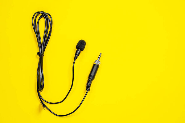 Shotgun microphone buttonhole for audio recorder, with wires, on bright yellow background. Sound record equipment.