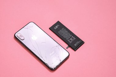 11 Nisan 2020, Rostov-on-Don, Rusya: cep telefonu ve taşınabilir cihazlar için lityum iyon bataryası ve pembe arka planda, üst görünümde bulunan kırık arka camlı akıllı telefon iPhone X.