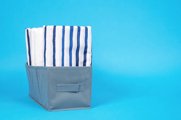 Stacks different white and striped bed linen on blue background. concept organized storage of clothes — Stock Photo, Image