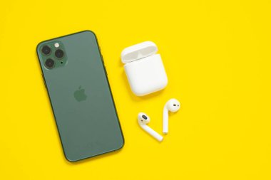 29 Nisan 2020, Rostov-on-Don, Rusya: Cep telefonu iPhone 11 Gece yarısı yeşil renkli Pro ve kablosuz kulaklıklar Sarı arka plan, üst görünüm, kopyalama alanı.