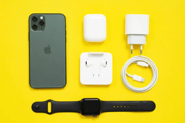 1 Mayıs 2020, Rostov, Rusya: Cep telefonu iPhone, kablosuz kulaklıklar kutuda çanta, Apple Watch S4 spor bandı, USB Lightning Cable ve güç adaptörü sarı arka plan, üst görünüm