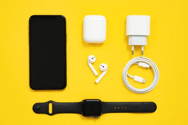 1 Mayıs 2020, Rostov, Rusya: Smartphone iPhone, kablosuz kulaklıklar çantalı AirPods, Apple Watch S4 spor bandı, USB Lightning Cable ve güç adaptörü sarı arka planda, üst görüş.