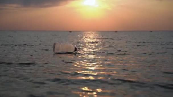 オープン海でのプラスチック製のボトルのドリフト、背景に美しい燃えるような夕日。自然破壊、環境汚染と水域汚染の地球規模の問題。消費の真の生態学のための緊急の必要性. — ストック動画