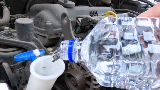 Człowiek wlewa wodę lub specjalny roztwór czyszczący z plastikowej butelki do spryskiwacza szyb samochodowych i zamyka pokrywę, zamyka. Niezależny nieprofesjonalny serwis samochodowy podczas podróży. — Wideo stockowe