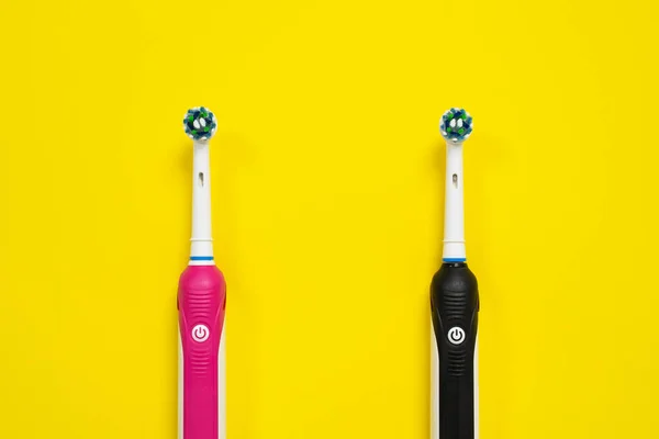 Μαύρο και ροζ ηλεκτρικές οδοντόβουρτσες με ανταλλακτικές κεφαλές, για αγόρι και κορίτσι σε κίτρινο φόντο, πάνω όψη, αντιγραφή χώρου. Σύγχρονες συσκευές καθημερινής υγειονομικής περίθαλψης, στοματικής υγιεινής. — Φωτογραφία Αρχείου