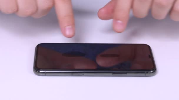 Homem instala vidro de proteção temperado inquebrável na tela frágil do novo smartphone, ele pressiona o protetor para a superfície da tela do telefone e suaviza as bolhas de ar com os dedos, de perto . — Vídeo de Stock