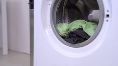 Mavi tişört ve kırmızı başlık giyen komik bir dachshund açık olan çamaşır makinesinin davul kapısından çamaşırları indirip kaçıyor. Köpek bakıcılığı mizah anlayışı.