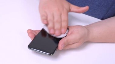 Bir adam cep telefonunun ekranını özel bir peçeteyle temizliyor.
