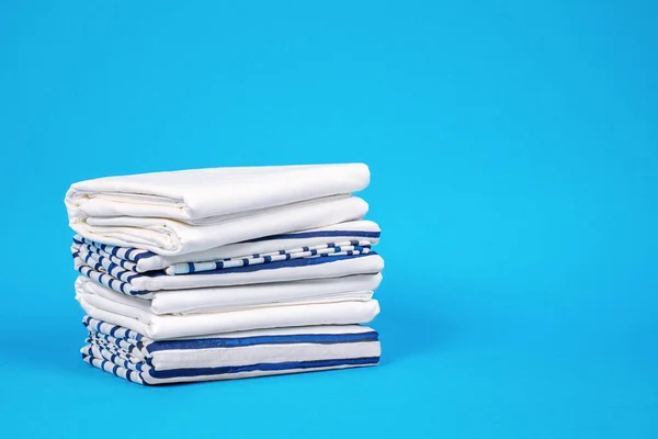 Asciugamani e biancheria da letto con soluzione di stoccaggio per armadio a casa. Federe e fogli ordinatamente impilati su sfondo blu, vista frontale, spazio copia per lettering . — Foto Stock