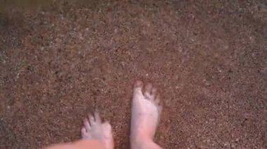 Denizde adım adım yürüyen çıplak insan ayakları ve dalgalarla yıkanan. Kumsal ve temiz şeffaf su, tatil beldesi konsepti.
