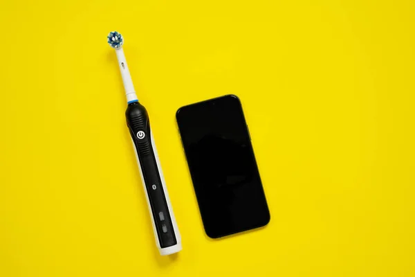 Modern electric toothbrush with replacement head and ability to automatically control and check data with smartphone application for daily dental healthcare on yellow background, top view, copy space. — Stock Photo, Image
