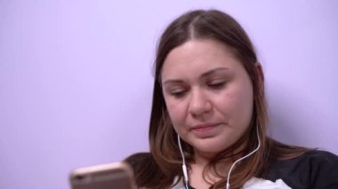 Genç kız gülümsüyor, mesajlar gönderiyor ve cep telefonuyla konuşuyor video çağrısı ve kulaklık kullanıyor ya da akıllı telefondaki uygulamadan kulaklıkla müzik dinliyor. Kadın serbest meslek sahibi evde çalışıyor..