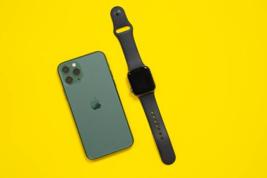 29 Nisan 2020, Rostov-on-Don, Rusya: Apple iPhone 11 gece yarısı yeşil renkli Pro ve arkasında üç kamera var. ve Apple Watch S5. İzole edilmiş, parlak sarı arka planda.