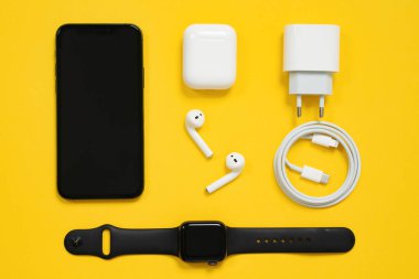1 Mayıs 2020, Rostov, Rusya: Apple cihazları, siyah iPhone ve AppleWatch seti, kutulu beyaz kulaklıklar, elektrik prizli, Apple yıldırımı C tipini kullanacak şekilde ayarlanmış, sarı zemin üzerinde katı çizgiler halinde dizilmiş.