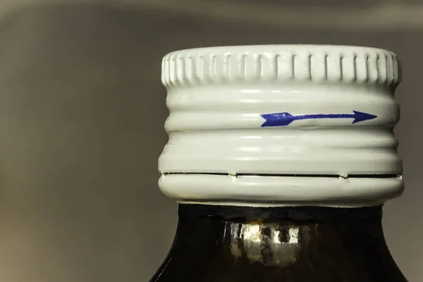 Makro fotoğraf tıp ve beyaz bir kapak ile karanlık bir şişe. Kapak tarafında mavi ok. Site hakkında tıp, sağlık.