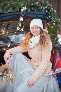 Gelin kız mavi bir arabanın bagajında oturuyor, kışın gelinin düğün buketini tutuyor.