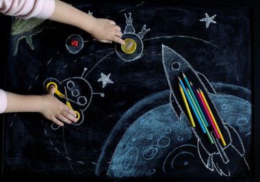 Roket, gezegenler ve yıldızlar kalem, bileyici ve makas yapılmış uzay tebeşir tahtası arka plan. Çocuk elleriyle yukarıdan görüntüle.
