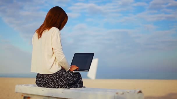 Jovem mulher usa o laptop touch pad enquanto sentado em um banco junto ao mar — Vídeo de Stock