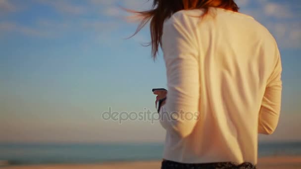 Fiatal nő a homokos tengerparton naplementekor a smartphone üzenet olvasása — Stock videók