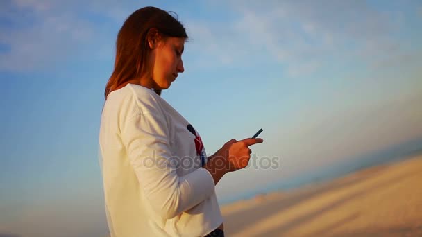 Schönes Mädchen benutzt ein Handy am Strand — Stockvideo