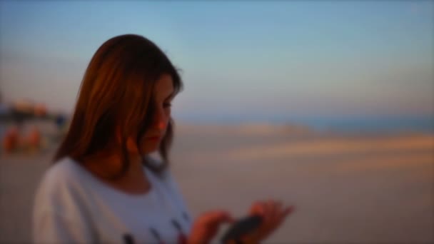 Fiatal nő használ egy okostelefon, este a tengerparton — Stock videók