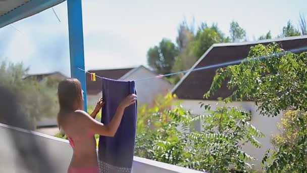 Jonge vrouw hangt een handdoek op een touw op zomerterras — Stockvideo