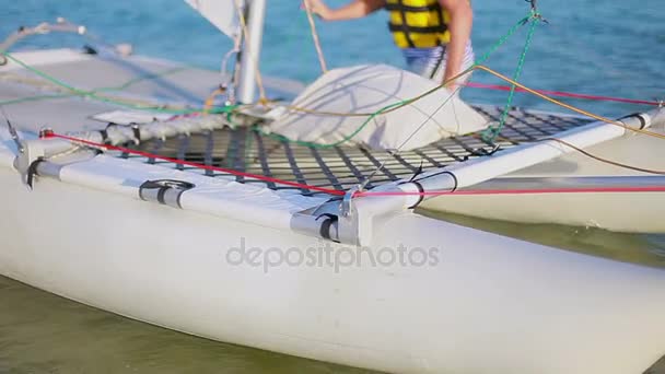 Equipo masculino y femenino trae un pequeño catamarán de vela en el mar — Vídeos de Stock