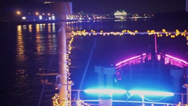 Barco de vacaciones iluminado flota en un río a lo largo de las luces nocturnas de la ciudad — Vídeo de stock