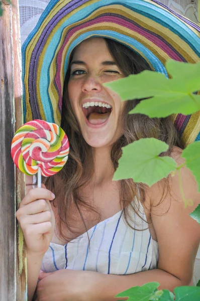 Fille drôle portant un chapeau coloré avec sucette dans la fenêtre avec des feuilles de raisin — Photo