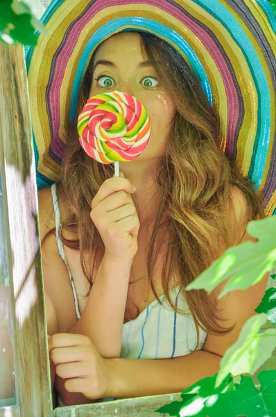 üzüm yaprakları ile penceresinde lolipop ile renkli bir şapka giymiş kız