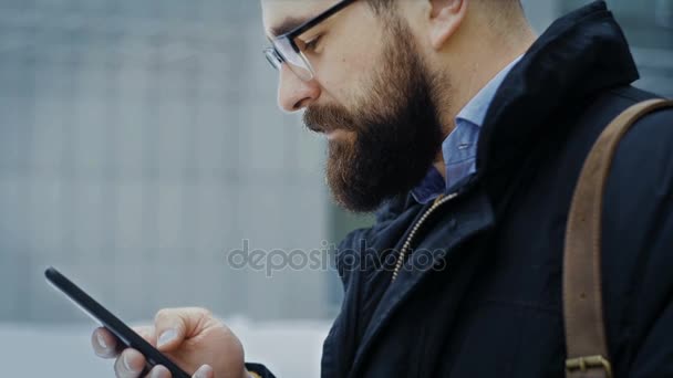 Кавказький людиною, в окулярах використовує смартфон на вулиці — стокове відео