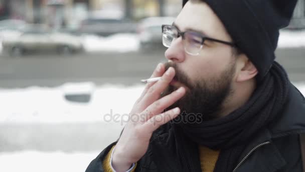 Человек в очках курит сигарету и пьет чай на городской улице — стоковое видео