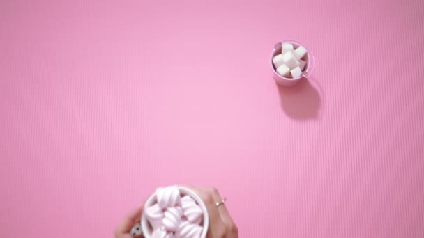 Руки девушки сверху берут чашку какао с зефиром из розового стола — стоковое видео